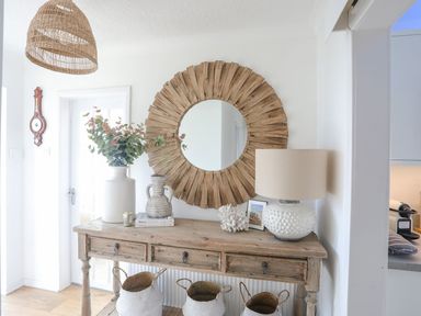 A wooden console table with decorative items below a round wooden mirror in a hallway at Trem Ynys 3 bed in Abersoch