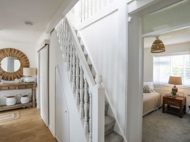 A staircase and hallway with a wooden console table and round mirror next to a bedroom with a bed and bedside table at Trem Ynys 3 bed in Abersoch
