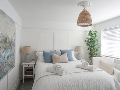 A bedroom with a bed with pillows and rolled towels bedside tables with lamps and a potted plant by the window at Trem Ynys 3 bed in Abersoch