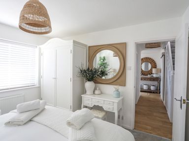 A bedroom with a white wardrobe white desk with a vase and mirror at Trem Ynys 3 bed in Abersoch