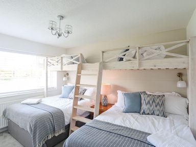 A bedroom with two double beds and a wooden bunk bed frame with ladder at Trem Ynys 3 bed in Abersoch