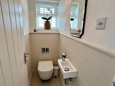 A small bathroom with a toilet a sink a mirror and a window with blinds at Trem Ynys 3 bed in Abersoch