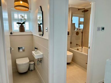 A small bathroom with a toilet sink and mirror next to a larger bathroom with a bathtub shower and toilet at Trem Ynys 3 bed in Abersoch
