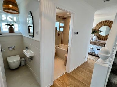 A hallway showing a small bathroom with a toilet and sink a bathroom with a bathtub and shower and an entrance to a room with a wooden console table and round mirror at Trem Ynys 3 bed in Abersoch