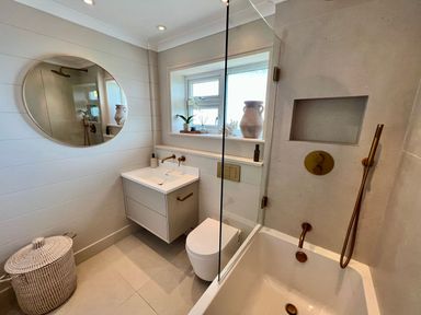 A bathroom with a bathtub shower combination sink toilet round mirror and window at Trem Ynys 3 bed in Abersoch