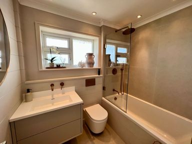 A bathroom with a bathtub shower combination a toilet and a sink under a window at Trem Ynys (3 bed) in Abersoch