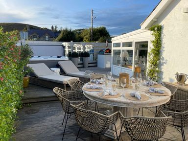 An outdoor deck with a round dining table set for six and two lounge chairs at Trem Ynys (3 bed) in Abersoch