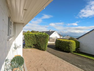 A driveway with potted plants next to a white building and trimmed hedges near houses at Trem Ynys 3 bed in Abersoch