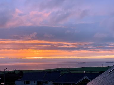A sunset over the sea with clouds and houses in the foreground at Trem Ynys 3 bed in Abersoch
