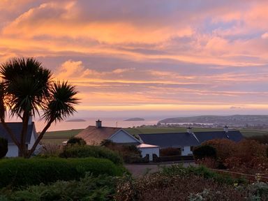 A view of houses trees and islands in the distance under a colorful sky at Trem Ynys (3 bed) in Abersoch