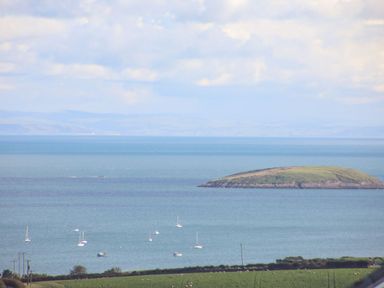 A coastal view with boats on the water and an island in the distance at Trem Ynys 3 bed in Abersoch