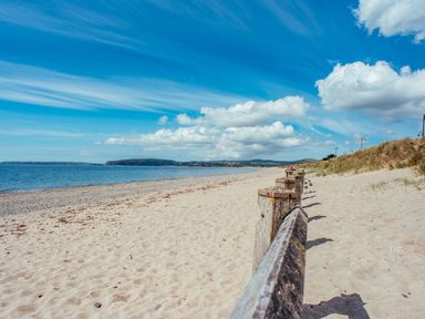 A sandy beach with wooden fencing along the side and a blue sky with clouds at Trem Ynys 3 bed in Abersoch