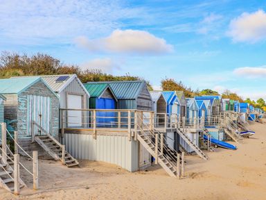 A row of beach huts with stairs on a sandy beach at Trem Ynys (3 bed) in Abersoch