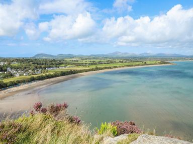 A coastal landscape with a sandy beach green fields and houses by the sea at Trem Ynys (3 bed) Abersoch