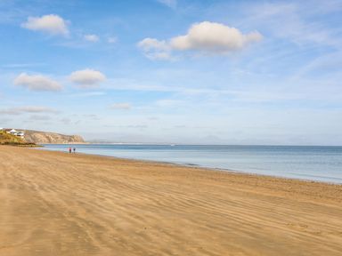 A sandy beach with two people walking near the water and cliffs in the distance at Trem Ynys 3 bed in Abersoch