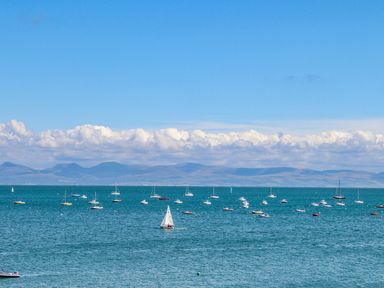 A body of water with multiple sailboats and yachts with hills and clouds in the background at Trem Ynys (3 bed) in Abersoch