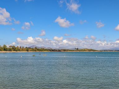 A view of a bay with small boats on the water and a coastline with trees and hills in the background at Trem Ynys 3 bed in Abersoch