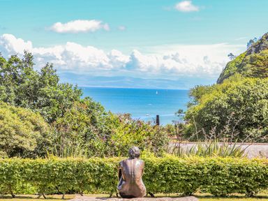 A garden with a statue of a seated person looking at the sea and a hill in the background at Trem Ynys 3 bed in Abersoch