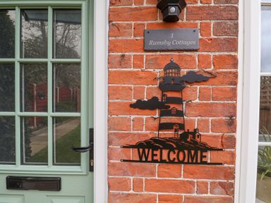 A green door next to a brick wall with a lighthouse welcome sign and a house number plaque at 1 Rumsby Cottages Gisleham near Kessingland