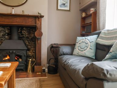 A living room with a wood burning stove fireplace a gray sofa with blue cushions and a wooden side table at 1 Rumsby Cottages Gisleham near Kessingland