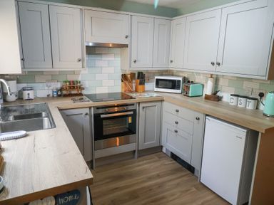 A kitchen with light wood countertops grey cabinets a stainless steel oven sink microwave toaster and small refrigerator at 1 Rumsby Cottages Gisleham near Kessingland