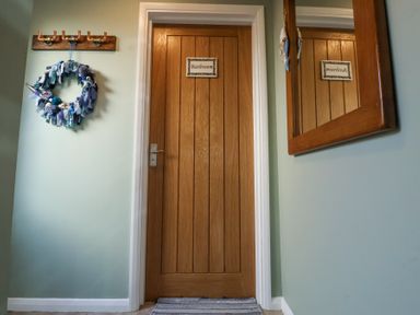 A wooden bathroom door with a sign a wall mirror and a coat rack with a blue wreath at 1 Rumsby Cottages Gisleham near Kessingland