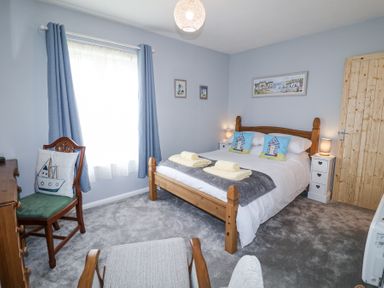 A bedroom with a wooden bed and bedside tables blue curtains and a wooden chair at 1 Rumsby Cottages Gisleham near Kessingland