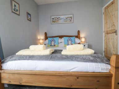 A bedroom with a wooden bed with two yellow towels on a grey blanket and two blue pillows on the bed at 1 Rumsby Cottages Gisleham near Kessingland