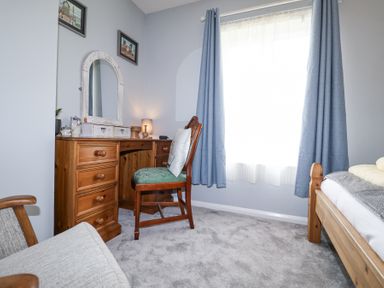 A bedroom with a wooden desk and chair next to a window with blue curtains at 1 Rumsby Cottages Gisleham near Kessingland