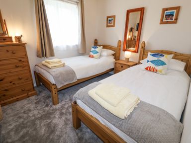 A bedroom with two single beds with fish-patterned pillows a wooden dresser a bedside table and a mirror at 1 Rumsby Cottages Gisleham near Kessingland