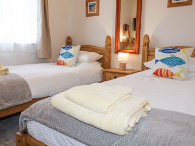 A bedroom with two single beds with fish patterned pillows and folded towels on one bed at 1 Rumsby Cottages in Gisleham near Kessingland