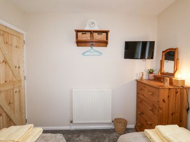 A bedroom with wooden dresser mirror flat screen tv and wall shelf at 1 Rumsby Cottages Gisleham near Kessingland