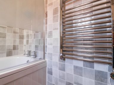 A bathroom with a bathtub and a chrome heated towel rail with tiled walls at 1 Rumsby Cottages in Gisleham near Kessingland