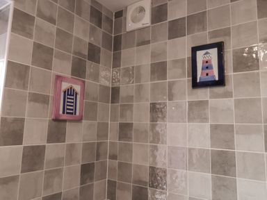 A corner of a tiled bathroom wall with two framed pictures and a ventilation fan at 1 Rumsby Cottages Gisleham near Kessingland