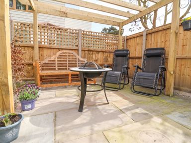An outdoor patio area with two black reclining chairs wooden bench fire pit table and potted plants at 1 Rumsby Cottages Gisleham near Kessingland