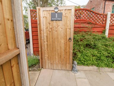 A wooden garden gate with a sign that says 1 Rumsby Cottages next to red fencing and green plants at 1 Rumsby Cottages in Gisleham near Kessingland