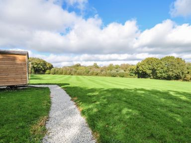 A gravel path leading to a wooden structure in a grassy field at Buzzards Lodge in Roche