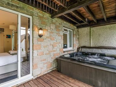 A covered outdoor area with a hot tub next to a stone wall and a door leading to a bedroom at 23 Valley Lodge in Gunnislake