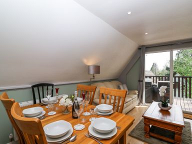 A dining table set with plates glasses and cutlery next to a beige sofa and a wooden coffee table with a plant by sliding glass doors at 23 Valley Lodge in Gunnislake