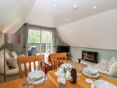 A dining and living area with a wooden table set for four and two sofas near a balcony at 23 Valley Lodge in Gunnislake