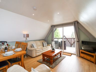 A living room with a beige sofa a wooden coffee table and dining table near a glass doors at 23 Valley Lodge in Gunnislake