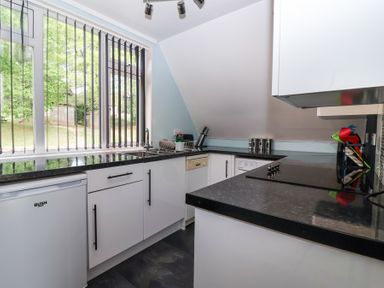 A kitchen with black countertops white cabinets a window with vertical blinds and kitchen appliances at 23 Valley Lodge Gunnislake