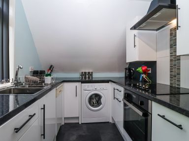 A kitchen with white cabinets black countertops a washing machine an oven a sink and various kitchen utensils at 23 Valley Lodge in Gunnislake