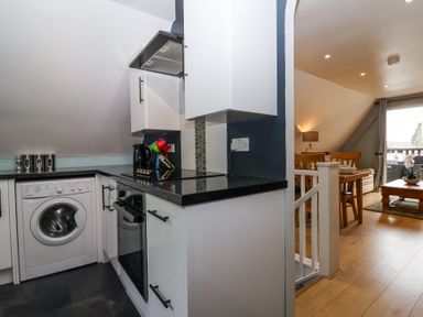 A kitchen area with washing machine oven and countertop next to a dining area with wooden table and chairs at 23 Valley Lodge in Gunnislake