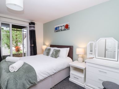 A bedroom with a double bed bedside tables with lamps a dresser with a mirror and a window with curtains at 23 Valley Lodge in Gunnislake