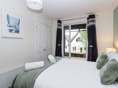 A bedroom with a bed with green pillows and blanket a radiator a wardrobe and glass doors with curtains at 23 Valley Lodge in Gunnislake