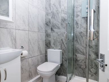 A bathroom with a toilet a sink a shower with glass doors and grey tiled walls at 23 Valley Lodge in Gunnislake