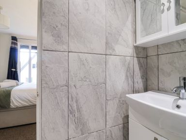 A bathroom sink with a mirror cabinet and tiled walls next to a bedroom with a bed and window at 23 Valley Lodge in Gunnislake