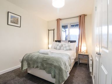 A bedroom with a bed with pillows and a rolled towel bedside tables lamps a mirror and curtains at 23 Valley Lodge in Gunnislake
