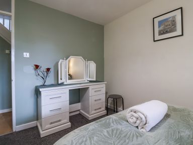 A bedroom with a white vanity dressing table with three mirrors a rolled towel on the bed and a framed picture on the wall at 23 Valley Lodge in Gunnislake